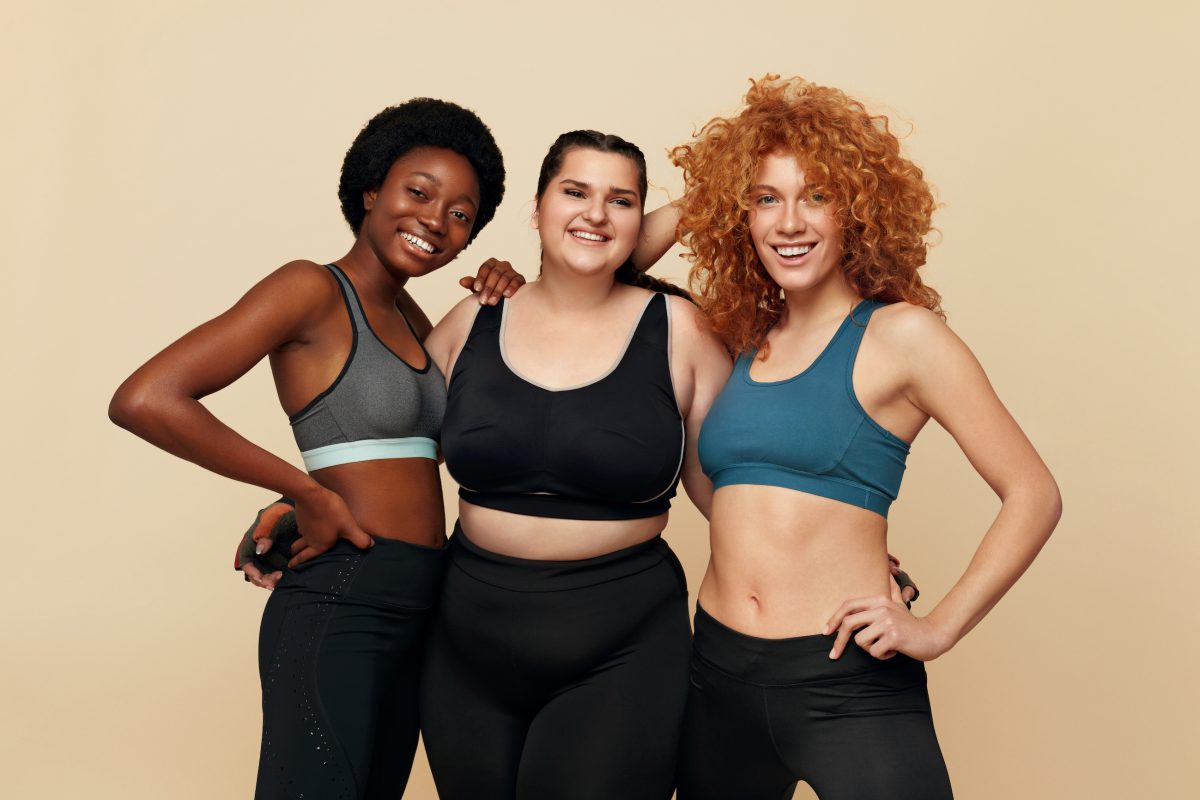 Different Women. Group Of Diversity Models Portrait. Smiling Multicultural Female In Fitness Clothes Posing On Beige Background. Body Positive As Lifestyle.
